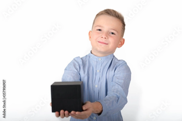 Fototapeta Smiling caucasian blond boy in blue shirt holds black box.the box is in front.Isolate white background.Close up.