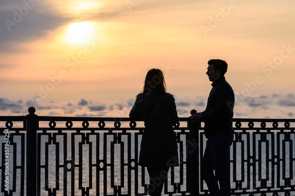 Fototapeta Two young people are talking while standing at sunset against the backdrop of the sea landscape