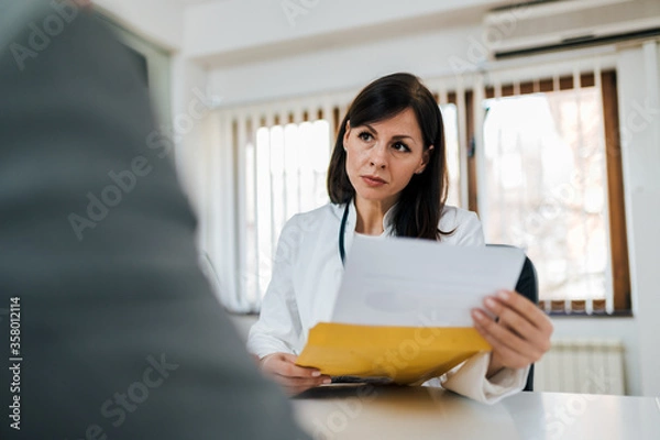 Fototapeta Portrait of a serious doctor looking at test results of a patient.