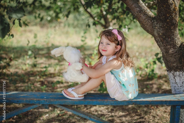 Fototapeta a girl with dark long hair sits on a bench legs up with a soft toy in her hands.