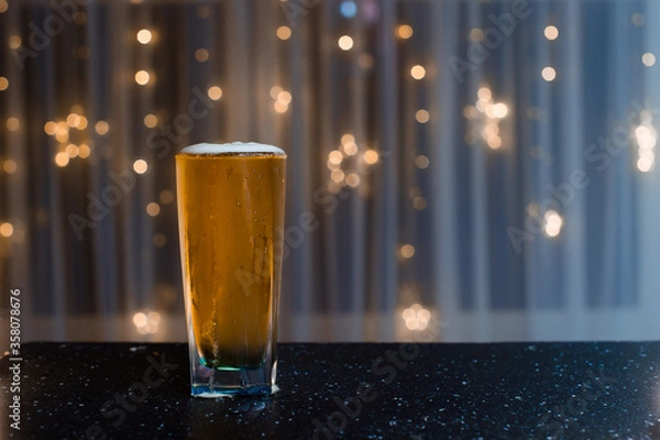 Fototapeta light beer in a figured glass on a black table on a blurred background