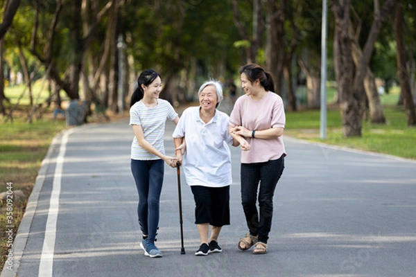 Obraz Happy asian family strolling embracing while relaxing and enjoying summer day in city park at leisure,smiling senior grandmother,mother,daughter child walking holding hand together along the promenade