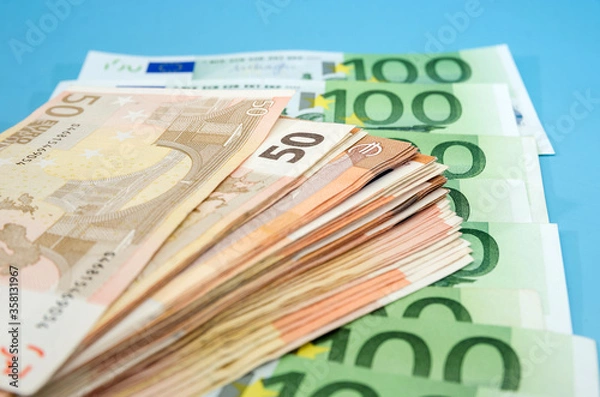 Fototapeta stack with 50 euros on the background of banknotes of 100 euros. Close-up. Financial concept. Blue background.
