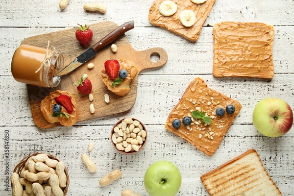 Fototapeta Bread with peanut butter, fruits and nuts on white wooden table