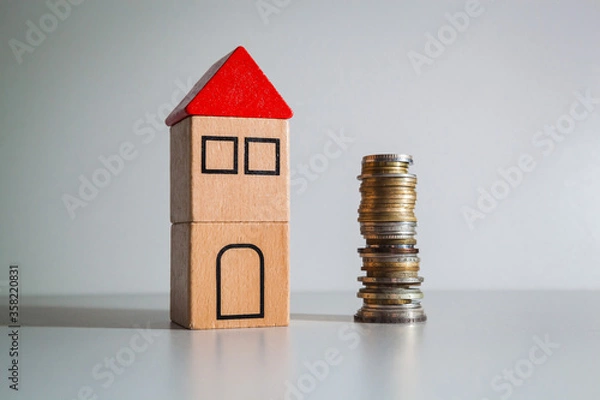 Fototapeta A wooden toy house with a red roof and a stack of coins.