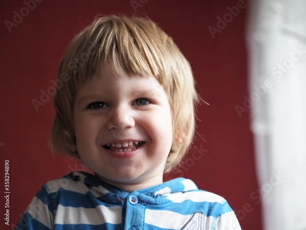 Fototapeta A child with light hair of European appearance smiles. The kid laughs sincerely while posing for the camera
