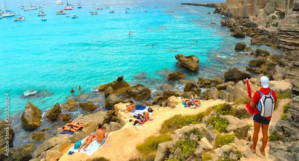 Fototapeta paradise clear torquoise blue water with boats and cloudy blue sky in background in Favignana island, Cala Rossa Beach, Sicily South Italy.