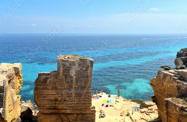 Fototapeta the rock cliff in front of paradise clear torquoise blue water with boats and cloudy blue sky in background in Favignana island, Cala Bue Marino Beach, Sicily South Italy.