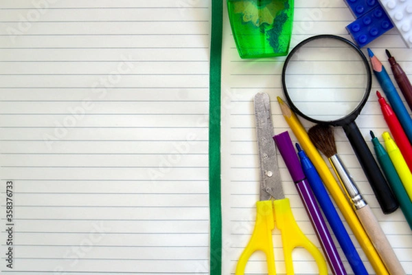 Fototapeta Back to school. Top view on a school desk with school subjects. Scissors, felt-tip pens, pencils, magnifying glass, open writing paper. Copy space