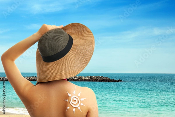 Fototapeta Young woman with sun protection cream on her back at beach, space for text