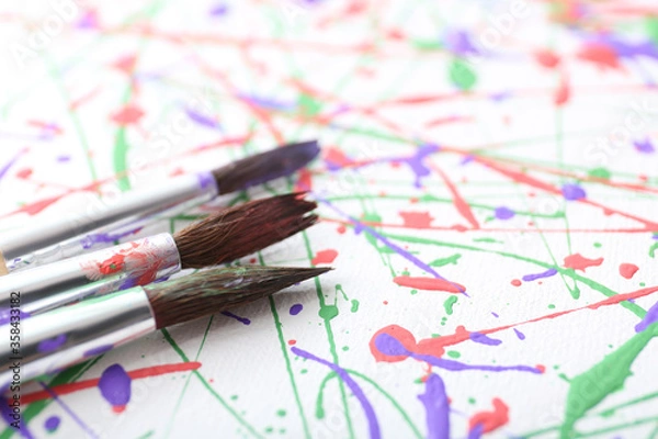 Fototapeta Brushes on canvas with colorful paint splashes, closeup. Art and creativity