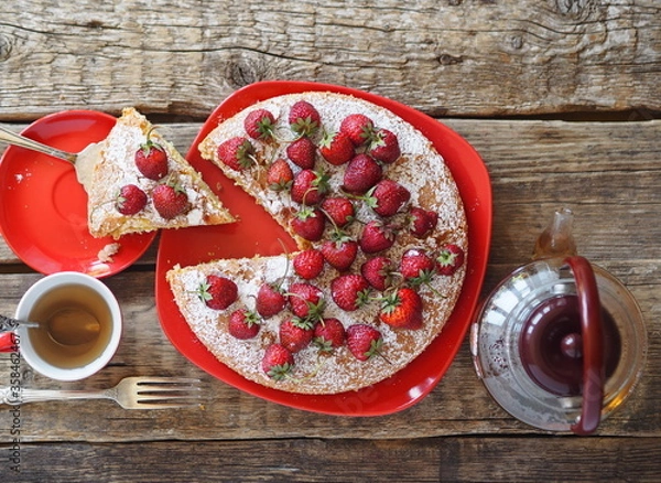 Fototapeta Confectionery background. Round pie with red strawberries on top on a red plate on a wooden natural background. Home cooking.