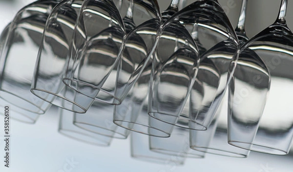 Fototapeta Close up detail view of many empty wine glasses hanging upside down on a special rack over the counter of a bar.