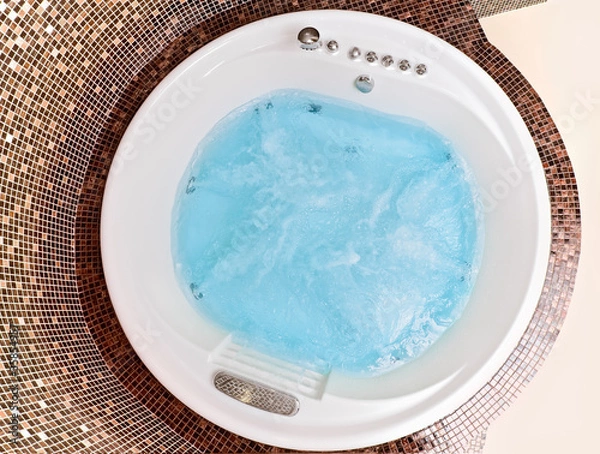Fototapeta White round jacuzzi with swirling water and brown mosaic in bath