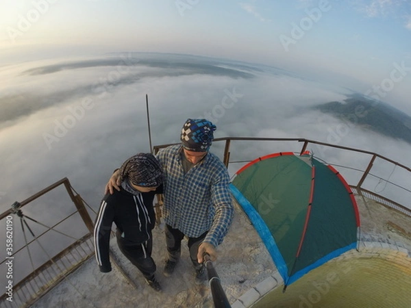 Fototapeta Camping on top of a smoke stack chimney, surrounded by fog and mist underneath the top of the building, sunrise