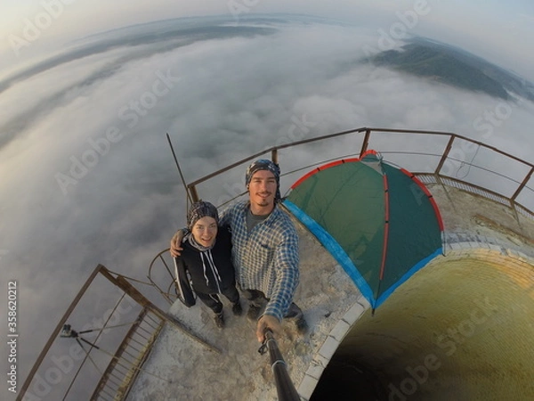 Fototapeta Camping on top of a smoke stack chimney, surrounded by fog and mist underneath the top of the building, sunrise