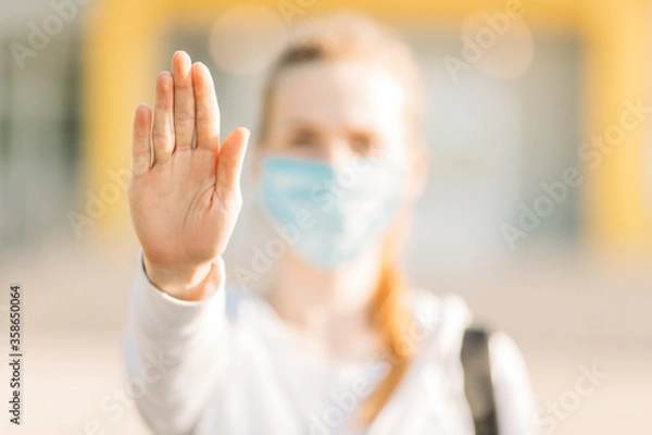 Fototapeta young woman in a medical protective mask stands in the open air and makes a stop gesture. Quarantine, coronavirus