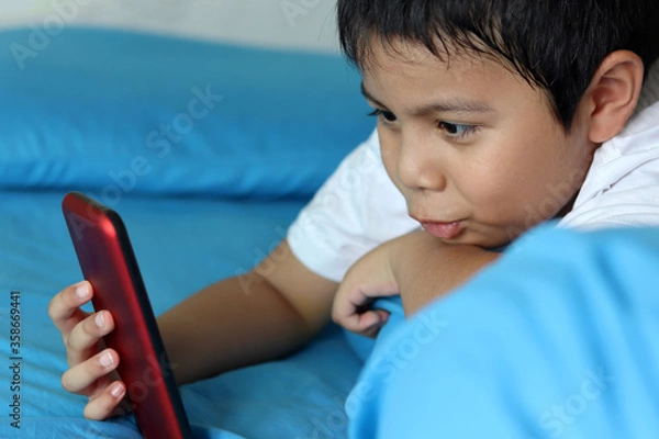 Obraz The boy playing games on smartphone. Child using a smartphone while lying on the bed. Social and technology concept.