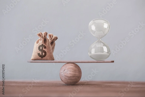 Fototapeta Financial concept : Write sand clock or hourglass symbol and dollar bagson a balance scale in equal position.Time value of money, asset growth over time, investment in long-term equity for more money 