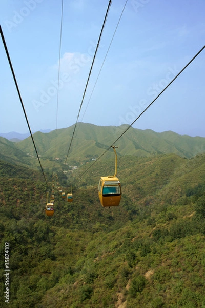 Fototapeta Cable cars traversing climb over green hills in summer