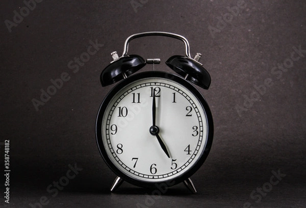 Obraz An old alarm clock showing 5 o'clock on a black background