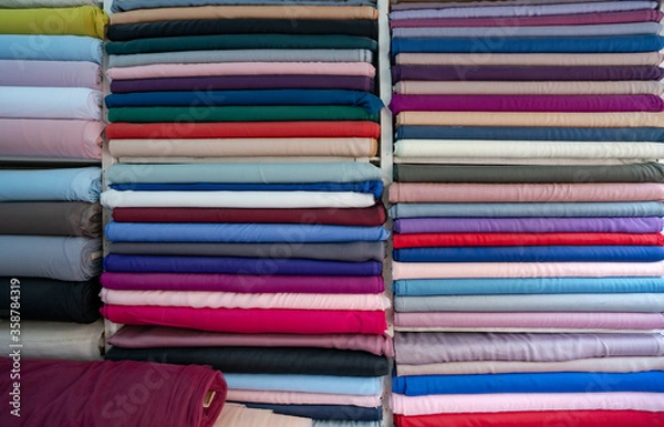 Fototapeta pile of colorful fabrics. haberdasher fabric shop choice of textile material in fabric market. Shelves with colorful fabric rolls. clothes in shop.