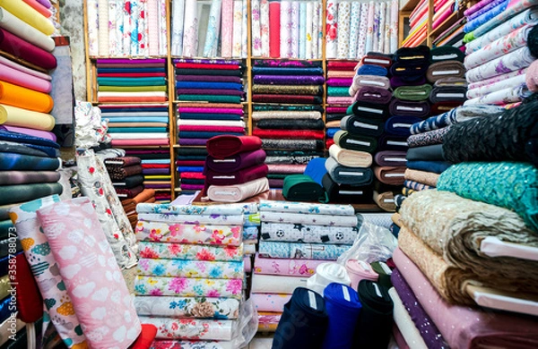 Fototapeta colorful scarves for sale. Clothes in shop, Rolls of fabric and textiles for sale stacked on shelves in shop, View of cloth rolls of different colors and patterns on shelves in fabric store