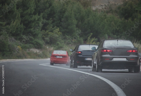 Fototapeta Multiple cars driving together in a column on a cold rainy day. Car enthusiast gathered and going for a road trip