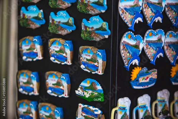 Fototapeta View of traditional tourist souvenirs and gifts from Calpe, Calp, Alicante, Valencia with toys, fridge magnets with and key ring keychain, in local vendor souvenir shop