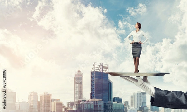 Fototapeta Confident elegant businesswoman presented on metal tray against cityscape background