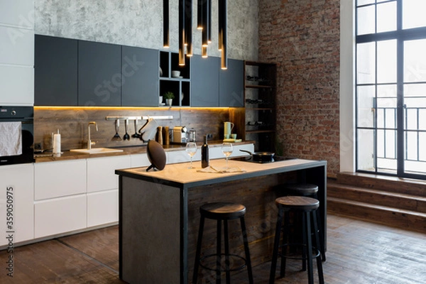 Obraz luxury studio apartment with a free layout in a loft style in dark colors. Stylish modern kitchen area with an island, cozy bedroom area with fireplace and personal gym
