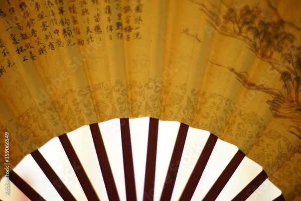Obraz yellow fan with brown chinese characters on it, white background, closeup.