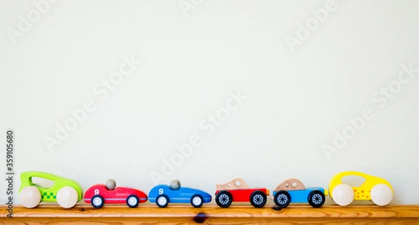Obraz a row of tiny wooden colorful  toy cars lined up along a child's bed headboard with copy space