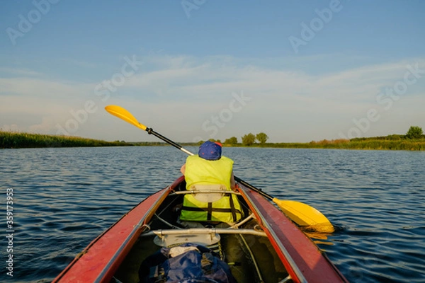 Fototapeta A little boy kayaks on the river in the summer and rowing an oar.