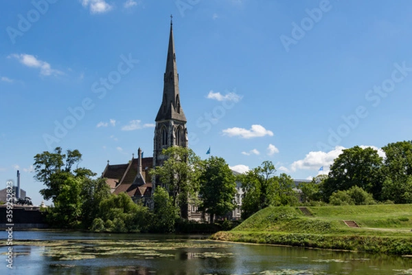 Fototapeta St Alban's English Church located next to the citadel Kastellet in Copenhagen, Denmark. Small lake in from of the church. Reflection in the water. Bright, sunny day.