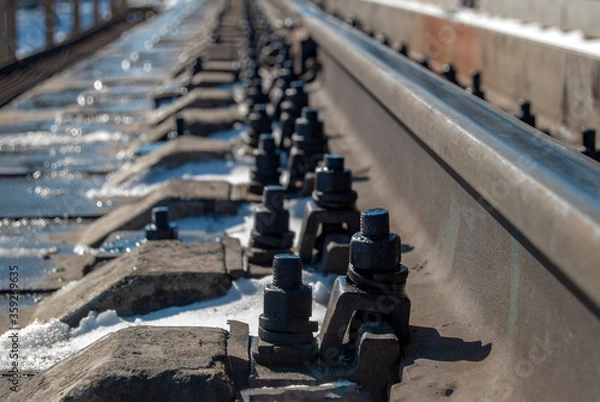 Obraz Fastening railway rails to sleepers. Focus on the first mounting bolt. Close-up. The device of the railway track.