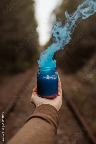 Fototapeta Blue colour smoke from a cup holded by a man hand on a forest