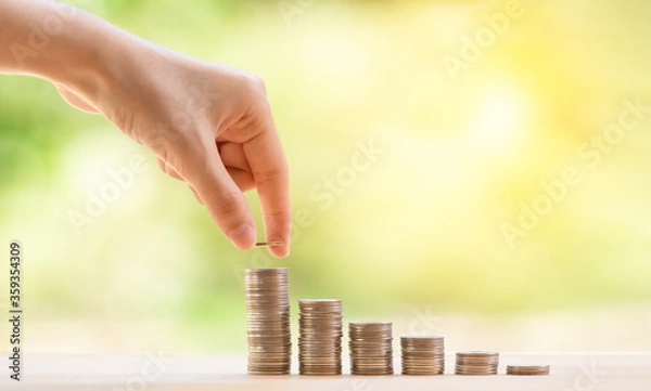 Fototapeta Hand putting cion on stact of cions step growing growth saving money on wooden panel nature green background, concept finance business investment.
