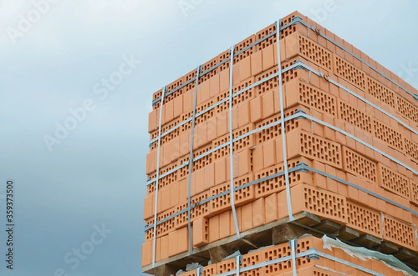 Fototapeta A tied bundle of lightweight red bricks against a blue cloudy sky closeup outdoors, on a wooden pallet.