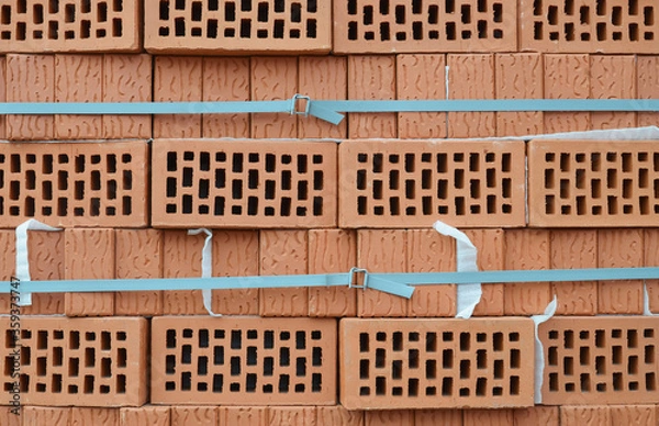Fototapeta The rough texture of the rows of red lightweight brick. View of the corrugated side and perforated upper surfaces of clay bricks. Two horizontal plastic tapes.