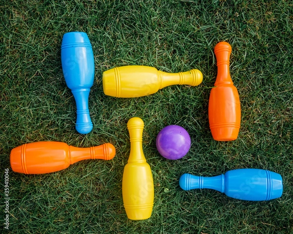 Fototapeta Children's set to play bowling on green grass. Ball and colored pins. Kid's game toy. Bowling colorful plastic pins. Active and interesting childhood concept.
