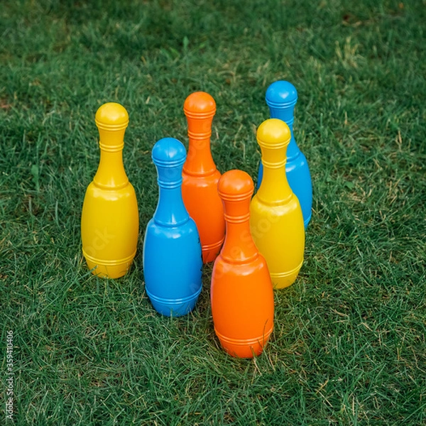 Fototapeta Children's set to play bowling on green grass. Ball and colored pins. Kid's game toy. Bowling colorful plastic pins. Active and interesting childhood concept.
