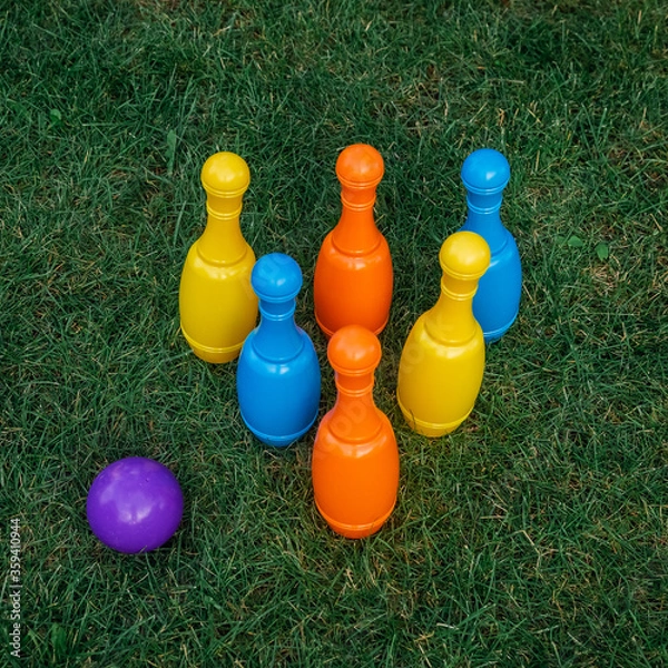 Fototapeta Children's set to play bowling on green grass. Ball and colored pins. Kid's game toy. Bowling colorful plastic pins. Active and interesting childhood concept.