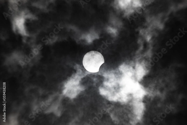 Obraz Partial solar eclipse close-up on a background of gloomy clouds.