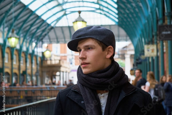 Fototapeta Young casual handsome guy wearing a brown scarf and a trendy gray ivy flat cap, visiting the interior of the former vegetable market of Covent Garden in London.