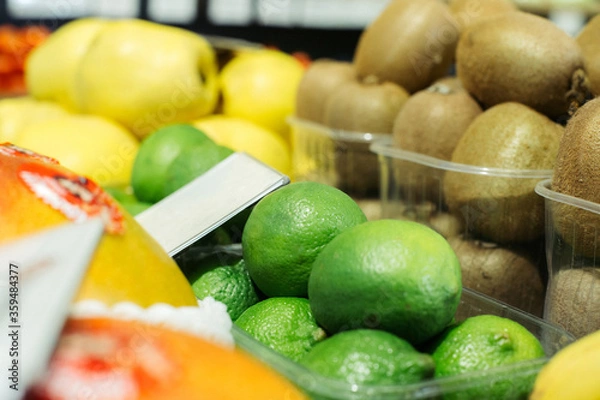 Fototapeta Green limes on shelf with blurred kiwi and pears at the background. Healthy vitamin eating, organic food, fruits in grocery..