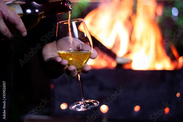 Obraz pour a glass of white wine from a bottle on the background of a barbecue with fire