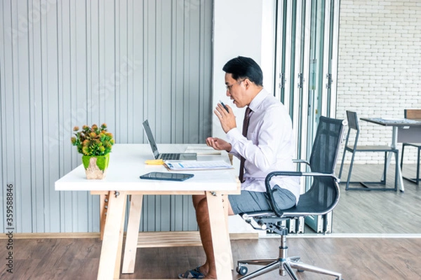 Fototapeta business man working from home in front of laptop on desk and wearing half of formal and casual outfit. contrast concept