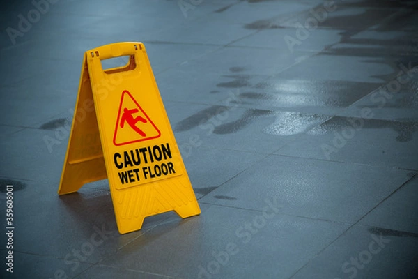 Fototapeta Yellow wet floor caution sign during rain with puddle of water when floor is slippery and copy space for text
