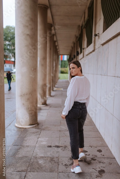 Fototapeta A beautiful young caucasian girl in front of a white building with pillars